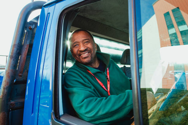 Senior truck driver is smiling while pulling out of a parking lot in his work truck.