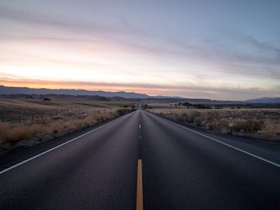 A shot of a highway road surrounded by dried grass fields under a sky during sunset