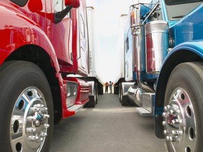 Truck drivers talking while standing between Class 8 trucks and trailers in a parking lot.